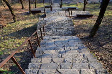 Dinlenme yerleri olan merdivenler. Parkta yamaçtan doğruca gölete gidiyor. Siyah metal korkulukları tutuyor. Taş doğa, beton yollar ve merdivenler. Lambalar ve ahşap banklar
