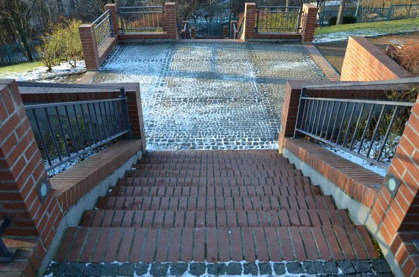 stairs and railings of exposed brick smooth surface. Metal railings and benches in the corners of the U-shaped brick retaining walls. The recessed lights illuminate the pedestrians\' feet under feet