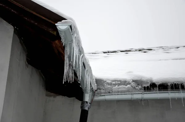 房子里的热量穿过屋顶融化了雪 它在屋顶的屋檐下结冰 形成冰柱 必须对桁架进行隔热处理 — 图库照片