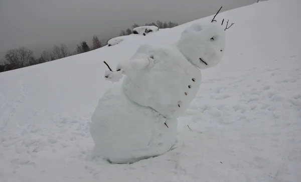 大きな雪だるまは体が傾斜していて体が倒れているようで足を滑らず腰痛を抱えています 冬は終わりだ 前かがみ — ストック写真