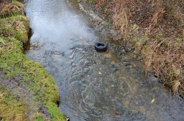 排水回灌渠道是降低地下水水位的一条过时的途径 灰色石头筑成的堤坝 向充满旧垃圾和汽车轮胎的田地提供灌溉用水 — 图库照片