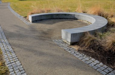 Japon uzun kuru otları kış için demetlere bağlandı. Parktaki granit bankın etrafını saran çiçek tarhının kemerinde. Bank at nalı gibi kıvrılmış, kaldırımın kenarında pürüzsüz bir yüzeyi var.