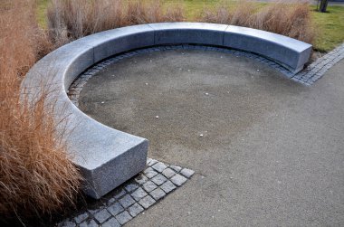 Japon uzun kuru otları kış için demetlere bağlandı. Parktaki granit bankın etrafını saran çiçek tarhının kemerinde. Bank at nalı gibi kıvrılmış, kaldırımın kenarında pürüzsüz bir yüzeyi var.