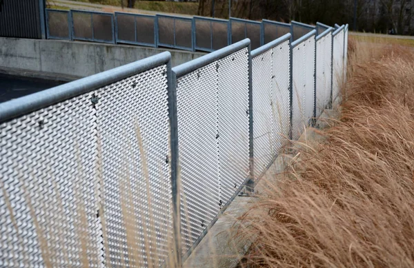 Genişletilmiş metal levha eskrimi. Galvanize parmaklıklardan yapılmış çok dayanıklı parmaklıklar. Süslü otların şeridi mekana insafsız bir bakış kazandırıyor. Öğütücü olarak yarı saydam