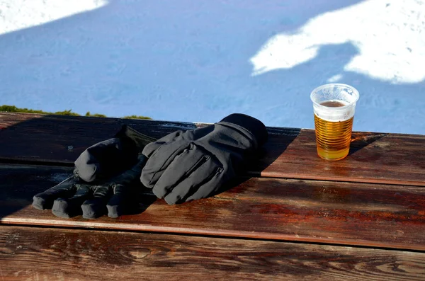 refreshments at the lift in the mountains. camping table with benches and soft pillows for rest and beer after skiing. beer in a mug and a snowmobile in the background. alcohol and driving