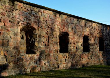 Kum taşından yapılmış anahtar deliği şeklinde delikleri olan gotik güçlendirme devresi. Kanalizasyon oluğu duvardaki yeraltı suyunu boşaltıyor. Çimenlikteki eski kayın