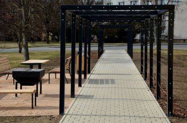 Otobüs durağının metal inşaatı, çardak pergola barınağı. Çatı ve duvarlar tırmanma tesisleri için bir halat ağıyla örülmüş. Paslanmaz çelik eşleşmelerle sabitlenmiş. siyah blok şekilli tünel,