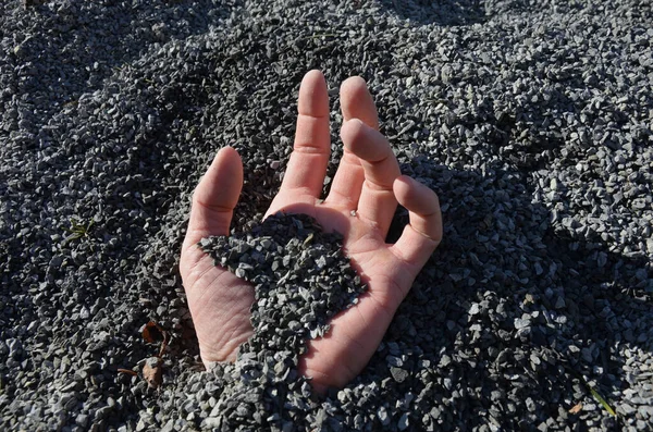 a man\'s hand buried in an accident that brings earthquakes or mining accidents. in fine gravel which is used for park construction of roads. fingers covered with sand in a pile dumped by a truck