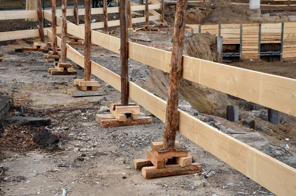 Tahtalardan yapılmış geçici ahşap çit şantiyesi. Kazı işleri ve temel çukurları bir çitle sınırlandırılmalı. Kazı makinesiyle büyük derinliğe kadar kazma, ezilmiş beton.