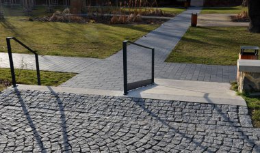 Hastane rampası devre dışı, betondan yapılma yuvarlak taşlar, ahşap merdiven bankı, merdivenlerde metal parmaklıklar, tekerlekli sandalye rampası.