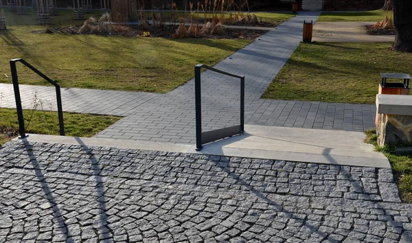 Hastane rampası devre dışı, betondan yapılma yuvarlak taşlar, ahşap merdiven bankı, merdivenlerde metal parmaklıklar, tekerlekli sandalye rampası.