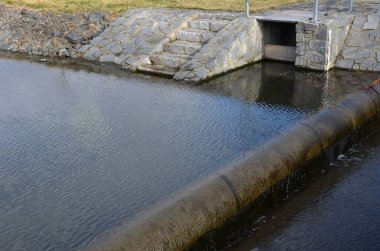 Barajın güvenlik açığı üzerine köprü. Gri düz taşların doğal asfaltlı taş köprüsü. Arzulama duvarlarının kenarında ince işlenmiş rengarenk demir parmaklıklar var. Su altından akar, taşar.