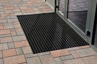 Binanın girişindeki endüstriyel paspas temizleme bölgeleri. Kemer ya da yarım daire şeklinde siyah plastik bir minder kireçtaşı mozaik fayansların üzerinde yatar.