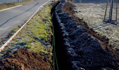 Yüksek voltajlı kablolar döşemek. Çevre elektrik direklerine zarar vermez. Siyah plastik kaplı, güçlü kablolarla kaplı bir kazı metresi. Elektrik şoku riski, telefon, açık hava, çimenlik