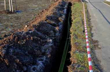 Yüksek voltajlı kablolar döşemek. Çevre elektrik direklerine zarar vermez. Siyah plastik kaplı, güçlü kablolarla kaplı bir kazı metresi. Elektrik şoku riski, telefon, açık hava, çimenlik