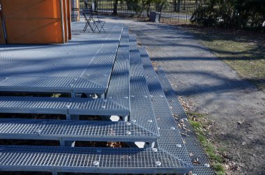 Metal merdivenler geniş ve şeffaf. Paslanmaz çelikten yapılmış. Park için uygun. Merdiven, doğa parkının kaldırımına, kahve masası ve sandalyeli bir terasa bağlanıyor.
