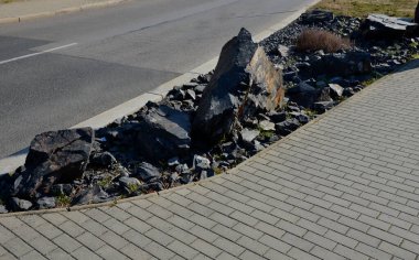 Sokakta park yerindeki kaldırım taşlarıyla çevrili çakıllı bir alan. çeşitli boyutlarda taş ocakları. Bitkisiz koyu gri kaya bahçeleri