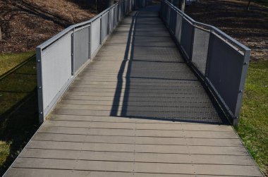 Tekerlekli sandalyeler, bisikletçiler ve bebek arabalı anneler için rampanın tahta pürüzsüz yüzeyi. Tahta kalaslar ve metal kafes parmaklıkları dolduruyor. Gri, bir köprü gibi yavaşça koşuyor. Binanın terası.