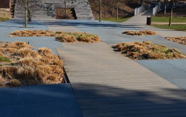 Pergola ve ahşap banklar ile gezinti güvertesinin beton pürüzsüz yüzeyi. Beton bazı yerlerde pürüzlü ve çizgiler var. Süslü, sade otlardan oluşan yataklar.