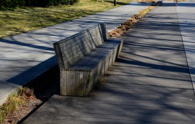 Pergola ve ahşap banklar ile gezinti güvertesinin beton pürüzsüz yüzeyi. Beton bazı yerlerde pürüzlü ve çizgiler var. Süslü, sade otlardan oluşan yataklar.