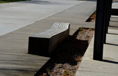 Pergola ve ahşap banklar ile gezinti güvertesinin beton pürüzsüz yüzeyi. Beton bazı yerlerde pürüzlü ve çizgiler var. Süslü, sade otlardan oluşan yataklar.