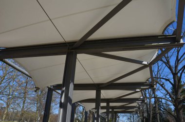 Beyaz tuval gerildi, güneşten gölgelendi ve restoranın terasına, anaokulundaki oyun parkına, gezinti platformuna yağmur yağdı. metalik gri kirişli pergola 