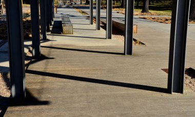 Pergola ve ahşap banklar ile gezinti güvertesinin beton pürüzsüz yüzeyi. Beton bazı yerlerde pürüzlü ve çizgiler var. Süslü, sade otlardan oluşan yataklar.