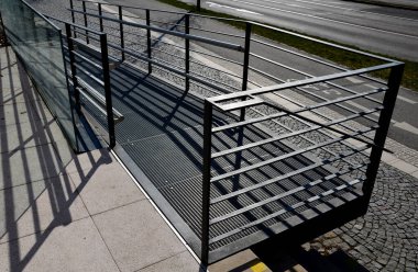 Tekerlekli sandalyeler, bisikletçiler ve bebek arabalı anneler için tel örgülü metal rampa. Tahta kalaslar ve metal kafes parmaklıkları dolduruyor. Gri, bir köprü gibi yavaşça koşuyor. Binanın terası.