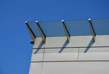 Endüstriyel binanın girişinin üstündeki cam çatı cephesinde metal kaplama var. Kalın duvarlı cam panel, metal çubukların üzerinde asılı. Yuvarlak hedef tutucuları, mavi gökyüzü.