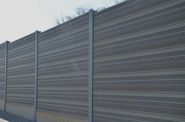 Metal delikli metal levhalardan oluşan ses bariyeri. Gri ve gümüşi koruyucu çitler gürültülü bir yoldan evleri ayırıyor. Gözenekli madde lastik sesini iyi parçalar..