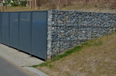 Gabion bahçesi, konteynırları yerleştirmek için kullanılıyor. Gri kapı ve delinmiş metal ızgaranın yarısı, genişletilmiş metal. Taştan sepetler dolduruldu ve çimenli yamaçlara gömüldü. Yaslananlar,