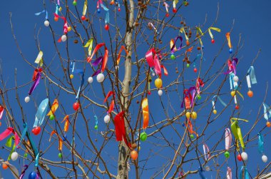 Paskalya ağacı, plastik yumurta süslemeleri ve çınar dallarında büyük miktarlarda asılı renkli kurdeleler. Mavi gökyüzü birlikte güzel bir klişe yaratıyor.