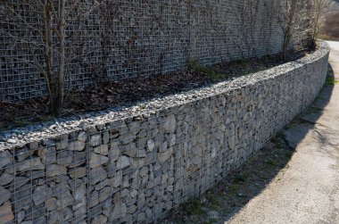 Ev çitlerinin bir parçası olarak bir Gabion istinat duvarı inşa etmek. İşçiler jeotextil koyuyorlar ve üzerine granit taşlardan oluşan tel sepetler koyuyorlar. El işi, teras talep ediyorlar.