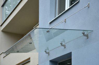 Endüstriyel binanın girişinin üstündeki cam çatı cephesinde metal kaplama var. Kalın duvarlı cam panel, metal çubuklarda, yuvarlak hedef tutucularla kapının üzerinde asılı.