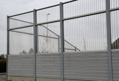 striped glass noise barrier made of metal perforated sheet metal slats. gray and silver protective fencing separates housing from a busy noisy road. the porous material shatters tire noise well. clipart