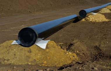 Bölgeye gaz boru hattı döşenmesi. Toprağın üst kısımlarını kazdık. Siyah boru toprak yığınları tarafından destekleniyor ve kazı alanının üzerinde kaynaklanıyor. Topraklama senkronize vinç ve asfalt tarafından gerçekleştirilir.