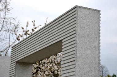Taş kaplama granit kaplamalı ve çizgili sırtlı kapı. Parkın ya da bahçenin girişinde. Gri sembolik bina, mavi gökyüzü. Değirmenli desenler, mezarlık