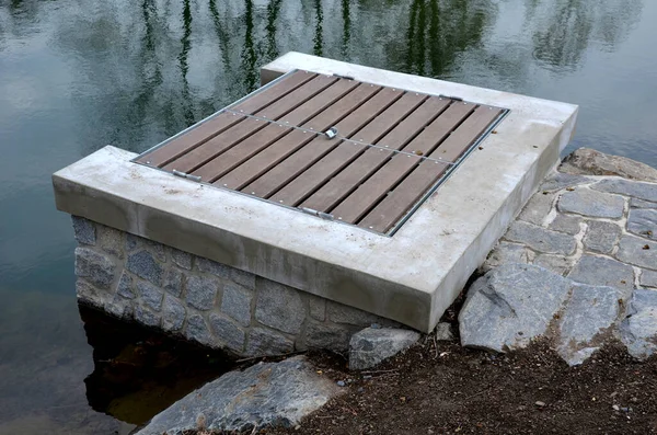 pond sluice, water reservoirs with regulation and concrete dam shaft. guide profiles determining flow, outflow under dam pipe. railing and bridge leading over water. service stone block  staircase