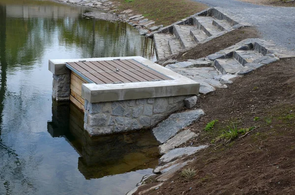 pond sluice, water reservoirs with regulation and concrete dam shaft. guide profiles determining flow, outflow under dam pipe. railing and bridge leading over water. service stone block  staircase
