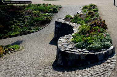 Granit tavan arası ve küçük eklemleri olan güzel katlanmış istinat duvarı. Kahverengi bej rengi düzensiz gneiss taşı üzerinde bir yamaç tutuyor. Etrafta talepsiz daimi varlıklar var.