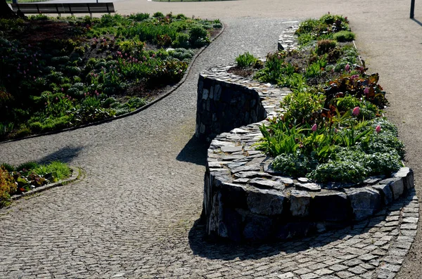 Granit tavan arası ve küçük eklemleri olan güzel katlanmış istinat duvarı. Kahverengi bej rengi düzensiz gneiss taşı üzerinde bir yamaç tutuyor. Etrafta talepsiz daimi varlıklar var.