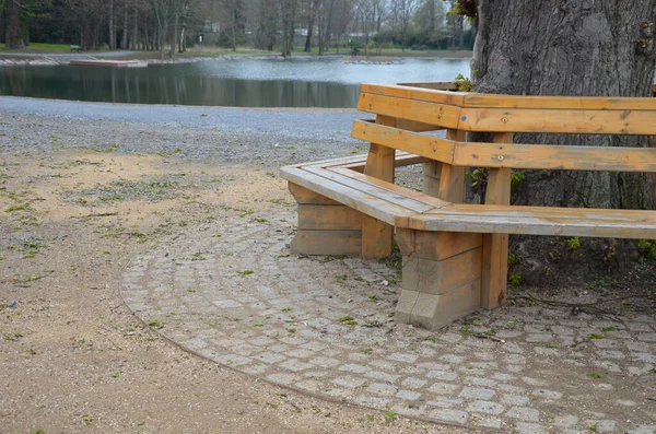 bench sitting round with wood paneling gray metal plate three seats around a tree around a gravel threshing path in the park lawn