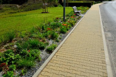 Çiçek yatağı lalelerden ve uzun ömürlülerden oluşuyor. Çimenliğin etrafındaki bej kaldırım boyunca uzanan uzun bir şerit. Şehir sokağı.