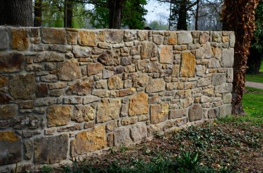 an old stone wall is being reconstructed between the two plots. the stones are dismantled and re-glued to the cement mortar. stonemason builds a wall in the park. the joints are repaired and the bush