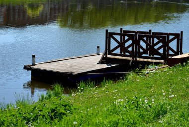 Park ziyaretçileri için iskele. İki adım ona götürür. Suyun üzerinde kalaslar var. Tekneler için rıhtımı olan bir gölet. Bir dikdörtgenin kat planı. Terasta parmaklık yok..