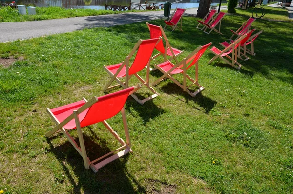 group of folding wooden hammock chairs on the lawn in foot in the alley in front of restaurant by the river on waterfront. the cycle path brings cyclists to cold drinks and rest. sunbathing girl