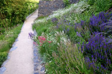 Yokuş aşağı kestirme yol. Yolun üstünde ve altında taş bir duvar var. Sonbahar parkında kanalizasyon ve metal şebeke ile doğa izleri. Her yıl kuraklık sarısı ile kaplanmış yamaçlar