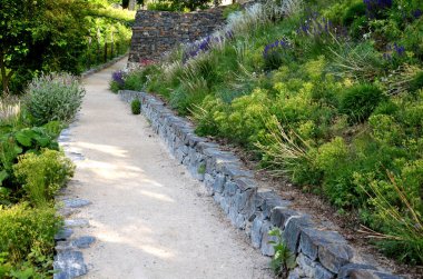Yokuş aşağı kestirme yol. Yolun üstünde ve altında taş bir duvar var. Sonbahar parkında kanalizasyon ve metal şebeke ile doğa izleri. Her yıl kuraklık sarısı ile kaplanmış yamaçlar