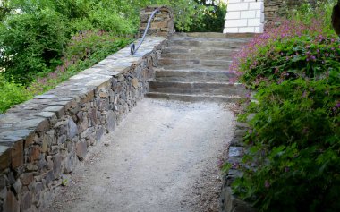 Sabah güneşiyle aydınlatılan taş merdiven. Taş kahverengidir ve çimento harcı ile birleştirilmiştir. Merdivenler kayalık bahçede ya da parkta.