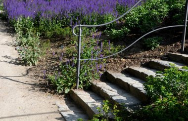 Siyah metalden dövülmüş korkuluklar yetenekli bir zanaatkârın ve atölyesinin işidir. Sapı bükülmüş. Çimlerin ve kaldırımın etrafında birkaç adım var.